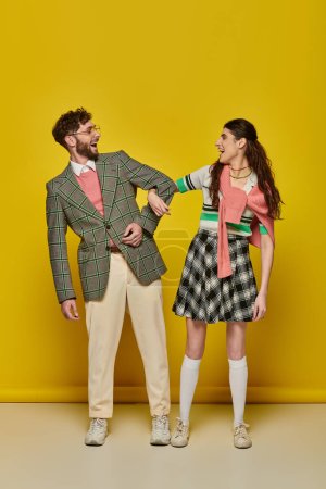 Foto de Estudiantes divertidos, pareja de pie sobre fondo amarillo, boca abierta, trajes universitarios, ropa académica - Imagen libre de derechos