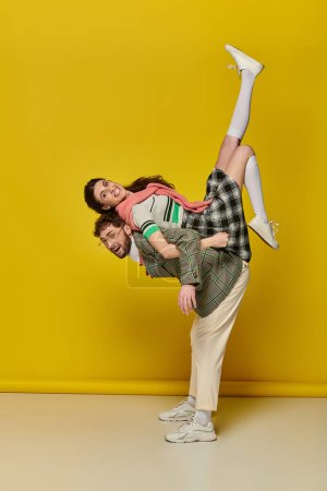 Photo for Funny couple, joyful man in glasses lifting woman, piggybacking, students in college wear, together - Royalty Free Image