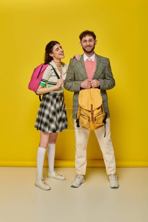 students standing with backpacks, looking at camera, smiling, yellow backdrop, academic wear, style