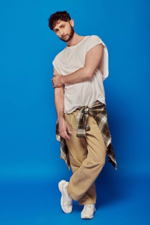 bearded man standing on blue background, tank top and pants, white sneakers, male fashion, style