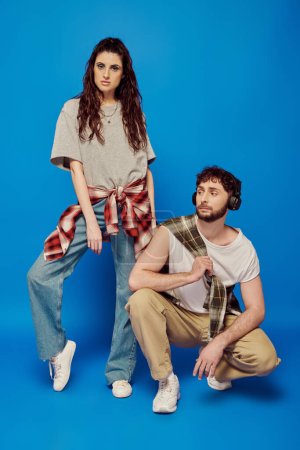 trendy couple, college students in casual attire, headphones, music, bold makeup, blue backdrop