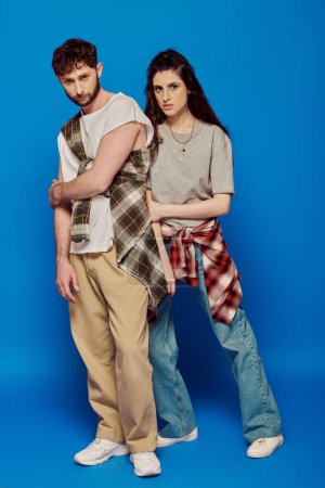 Paar posiert in Streetwear, blauer Hintergrund, Frau mit fettem Make-up steht mit bärtigem Mann, Stil