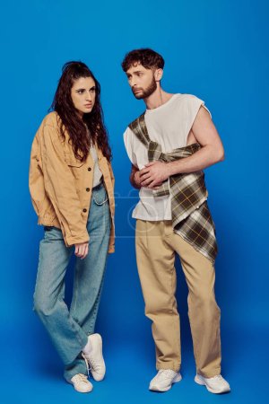 Photo for Fashionable couple, casual wear, posing on blue backdrop, bearded man, brunette woman, bold makeup - Royalty Free Image