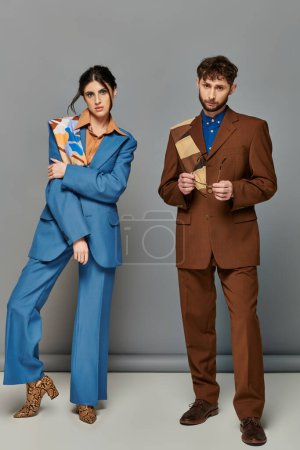 hombre y mujer en trajes a medida, de pie sobre fondo gris, sesión de fotos de moda, pareja, mira a la cámara