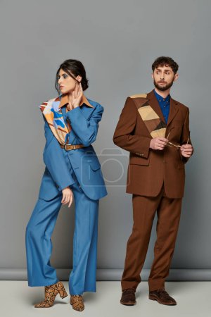man and woman in tailored suits, standing on grey backdrop, fashion shoot, corporate style, couple