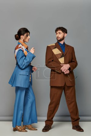 Téléchargez les photos : Homme et femme élégants en costumes sur mesure, debout sur fond gris, tournage de mode, couple, modèles - en image libre de droit