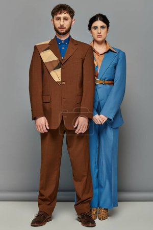pareja elegante posando en trajes a medida, atuendo formal, fondo gris, moda, mirando a la cámara