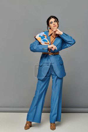 schöne Frau mit kühnem Make-up, Modell im blauen Maßanzug, formelle Kleidung, grauer Hintergrund