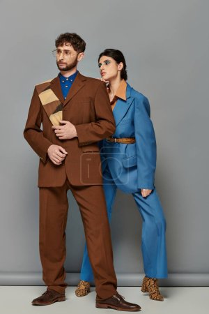modelos de moda en trajes posando sobre fondo gris, elegante hombre y mujer en traje formal a medida