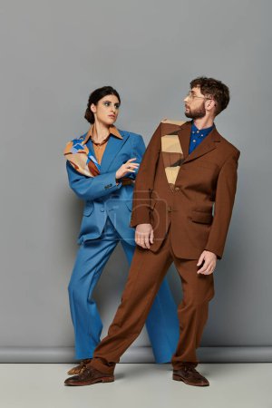 modelos de moda en trajes posando sobre fondo gris, hombre y mujer chic mirándose