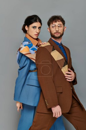 stylish couple in suits posing on grey background, elegant style, bold makeup, man and woman