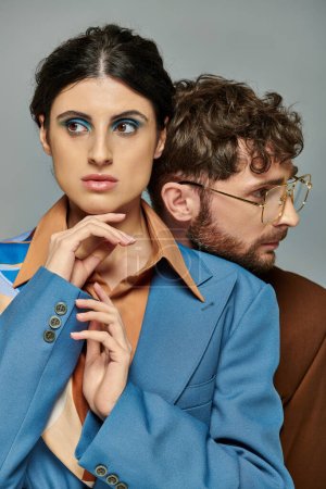Trendpaar posiert auf grauem Hintergrund, Anzüge, eleganter Stil, Frau mit kühnem Make-up, bärtiger Mann