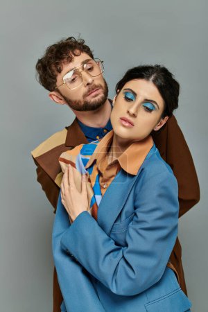 portrait of bearded man in glasses near woman, fashion models in trendy suits, grey background