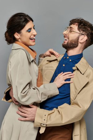temporada de otoño, hombre y mujer alegre abrazándose sobre fondo gris, pareja en abrigos de trinchera, estilo, romance
