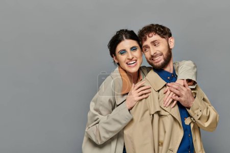 Foto de Temporada de otoño, sonrisa, pareja romántica abrazándose sobre fondo gris, abrigos de trinchera, estilo, romance - Imagen libre de derechos