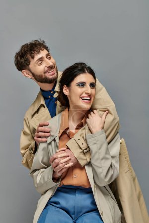 Foto de Pareja alegre, ropa de abrigo, temporada de otoño, fondo gris, hombre y mujer en gabardina, estilo - Imagen libre de derechos