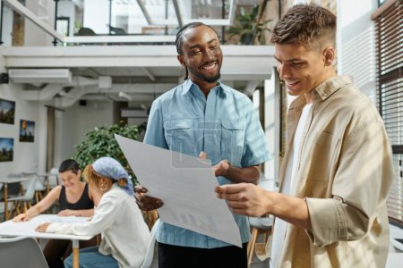 cheerful interracial men looking at project on paper, office workers smiling near female colleagues