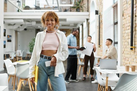 positive afrikanisch-amerikanische Frau mit Zahnspange, die Smartphone, Ordner, Startup, Gen z, Coworking hält