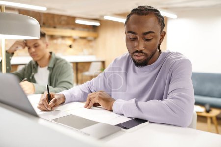 Coworking, afrikanisch-amerikanischer Mann macht Notizen, schreibt Ideen in der Nähe von Gadgets auf, Startup-Planung