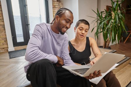 african american man showing project on laptop to woman, startup planning, ideas, coworking, gen z