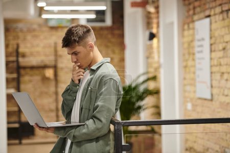 pensive man using laptop, standing in modern coworking, office environment, generation z, startup