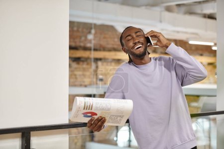 joyful african american man talking on smartphone, laughing, startup, holding graphs, digital