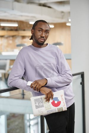 african american man holding smartphone and graphs, looking at camera, generation z, startup