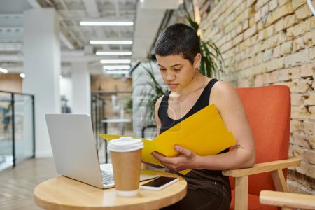young businesswoman sitting near table with gadgets, looking at folder, startup project, gen z