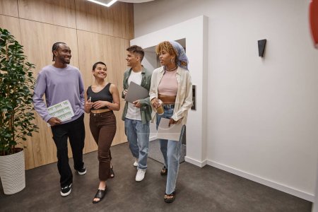 Foto de Diversidad cultural, felices colegas interracial caminando juntos en el coworking moderno, startup - Imagen libre de derechos