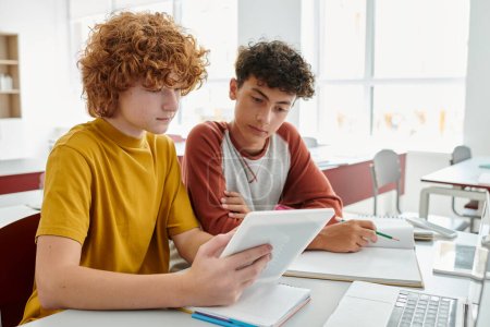 Téléchargez les photos : Les écoliers adolescents utilisant une tablette numérique ensemble près des ordinateurs portables sur le bureau pendant les cours en classe - en image libre de droit