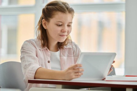 Escolar adolescente sonriente con ropa casual usando tableta digital durante la lección en el aula