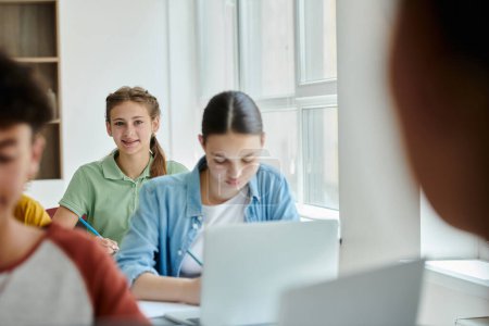 Teenager Schulmädchen schaut in die Kamera und lächelt in der Nähe verschwommener Klassenkameraden während des Unterrichts im Klassenzimmer