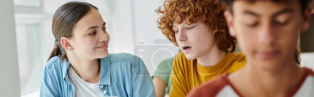 Photo for Smiling teenage schoolgirl looking at classmate talking during lesson in classroom in school, banner - Royalty Free Image