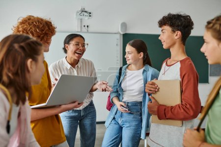 fröhliche afrikanisch-amerikanische Lehrerin lacht mit Teenagern im Klassenzimmer, zurück in die Schule