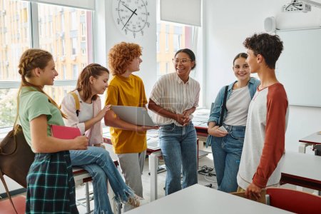 estudiantes adolescentes sonriendo cerca del profesor afroamericano en el aula, mujer negra, de vuelta a la escuela