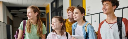 Foto de Pancarta, escolares adolescentes felices mirando hacia otro lado y de pie en el pasillo de la escuela, compañeros de clase adolescentes - Imagen libre de derechos