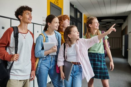 Photo for Happy teenage schoolkids looking away in school hallway, teen girl pointing with finger away - Royalty Free Image
