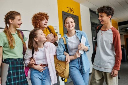 Téléchargez les photos : Adolescents écoliers rire et debout dans le couloir de l'école ensemble, des camarades de classe adolescentes avec des appareils - en image libre de droit