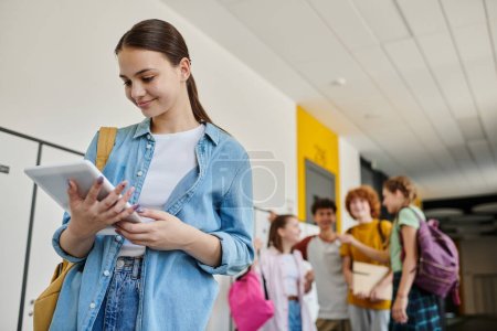 Téléchargez les photos : Heureuse écolière utilisant tablette numérique pendant la pause dans le couloir de l'école, floue, écoliers - en image libre de droit