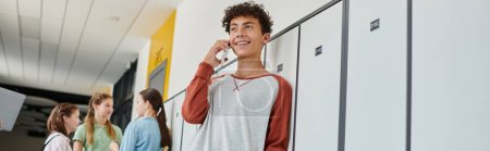 Téléchargez les photos : Bannière, écolier heureux avec bretelles ayant un appel téléphonique, parler sur smartphone dans le couloir de l'école, flou - en image libre de droit