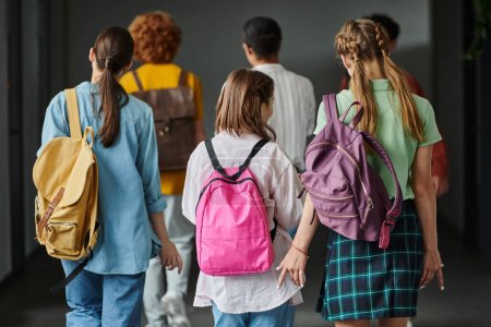 back view of schoolkids walking in hallway of school between classes, teen students, back to school