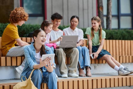 Téléchargez les photos : Retour à l'école, jeune fille tenant une tablette numérique et riant en plein air, e-study, diversité, étudiants - en image libre de droit