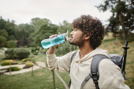Photo for Side view of indian traveler with backpack drinking water with landscape on background - Royalty Free Image
