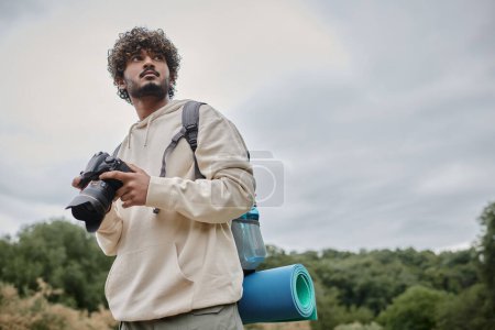 fotógrafo indio rizado en sudadera con capucha con cámara profesional, viaje y concepto de aventura