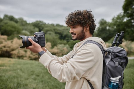 curly indian photographer with backpack taking shot on professional camera, adventure and hiking