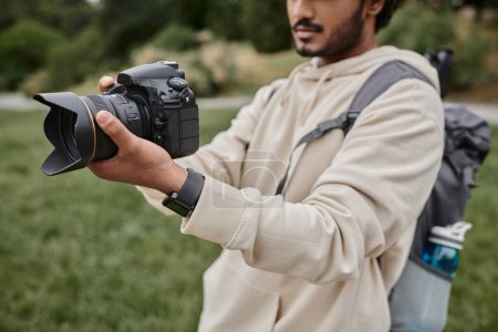abgeschnittene Ansicht eines indischen Fotografen mit Rucksack, der mit professioneller Kamera fotografiert wird, Abenteuer
