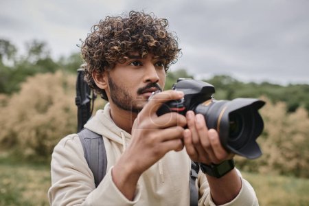 Konzentrierter indischer Fotograf mit professioneller Kamera und Fotografieren in natürlicher Umgebung