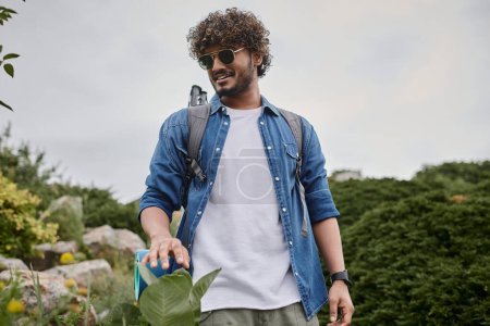 Téléchargez les photos : Nature sauvage, heureux homme indien en lunettes de soleil marche avec sac à dos sur la colline, randonneur ayant voyage - en image libre de droit