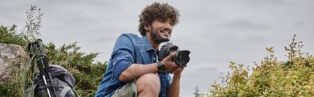 travel photographer concept, happy indian man taking photo on digital camera in natural place