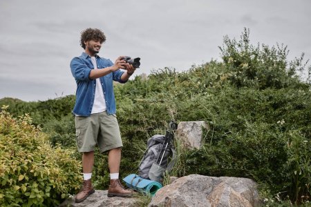 Téléchargez les photos : Concept d'aventure et de photographie, heureux homme indien prenant des photos à l'appareil photo dans un lieu naturel, bannière - en image libre de droit